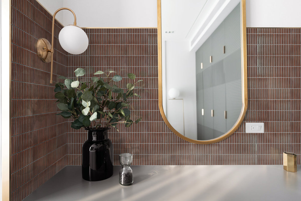 Burgundy finger mosaic tiles with contrasting grey grout beside a gold-framed bathroom mirror