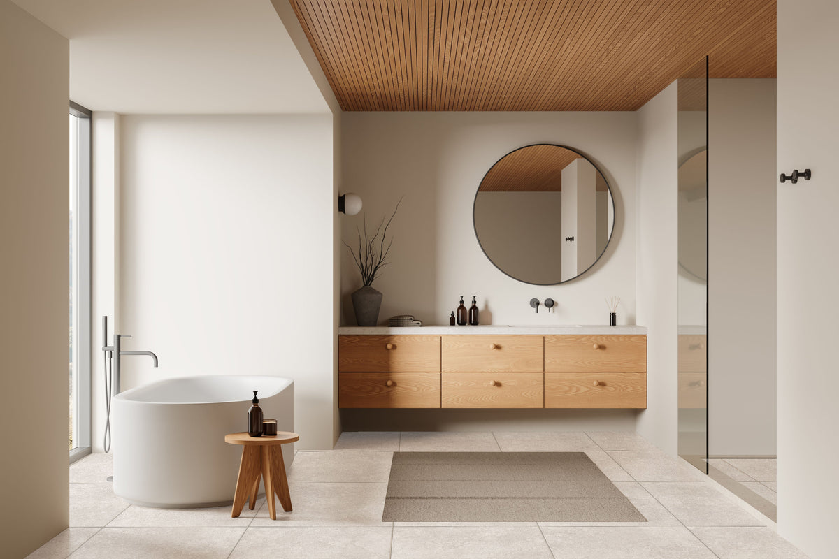Modern bathroom with pale floor tiles, floating timber vanity, round mirror and freestanding bath