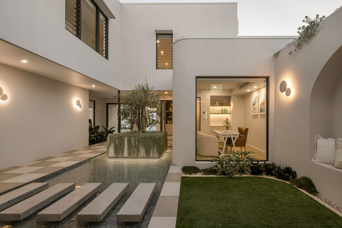 Contemporary courtyard entrance featuring floating concrete stepping stones across a shallow reflective water feature, framed by modern architecture and landscaped greenery.
