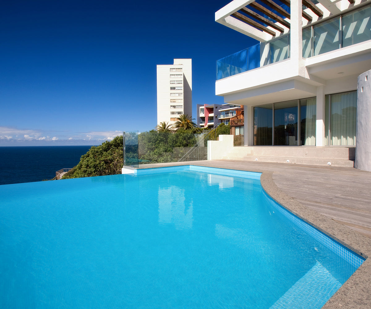 Luxury beachfront infinity pool featuring shimmering blue mosaic tiles, crystal-clear water and uninterrupted ocean views beside a contemporary coastal residence.