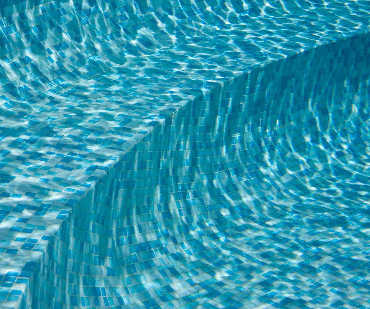 Close-up of shimmering blue mosaic pool tiles beneath crystal-clear water, showcasing the rich colour variation and light-reflecting finish of a luxury swimming pool.