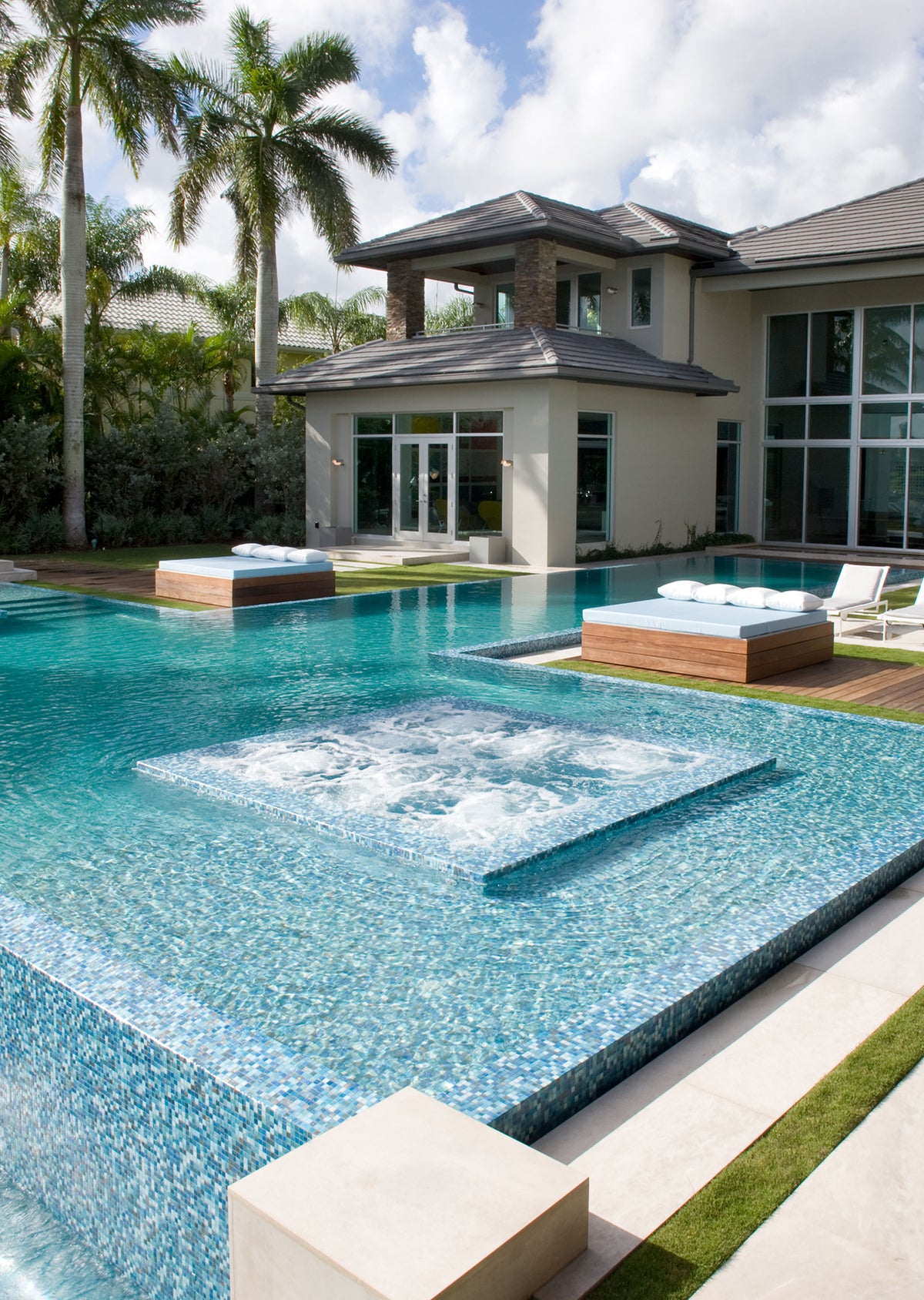 Luxury swimming pool finished with blue mosaic tiles, featuring a raised spa platform with bubbling jets, crystal-clear water and a resort-style tropical setting.