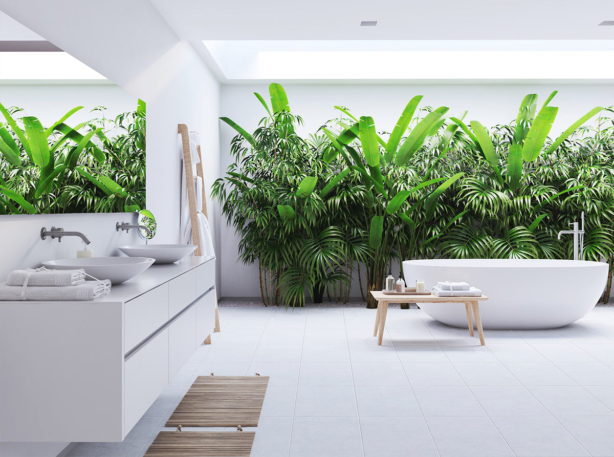 A modern white bathroom with a double-sink vanity, a freestanding oval bathtub, and a large wall mural or panel of lush green tropical plants behind the tub.