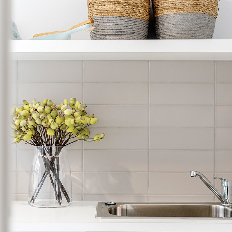 Laundry room featuring a white tiled splashback, stainless steel sink, open shelving and woven storage baskets, creating a clean and functional utility space.