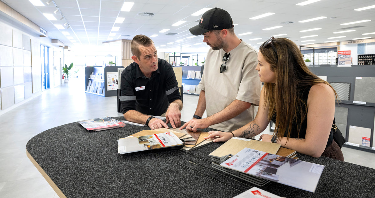 Customers receiving expert advice from a Beaumont Tiles consultant while comparing hard flooring samples and product options in a modern showroom.