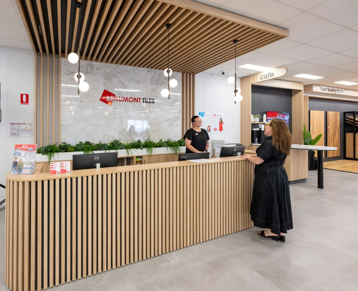 Customer speaking with a Beaumont Tiles team member at the showroom reception desk, featuring timber battens, pendant lighting and tile display areas.