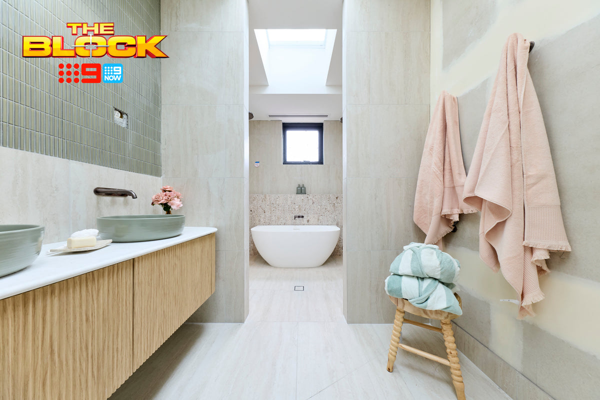 The Block House 1 main ensuite featuring soft stone-look floor and wall tiles, a floating timber vanity with sage green vessel basins, textured green feature wall tiles, freestanding bath, skylight, and pastel styling accents creating a calm spa-inspired bathroom.