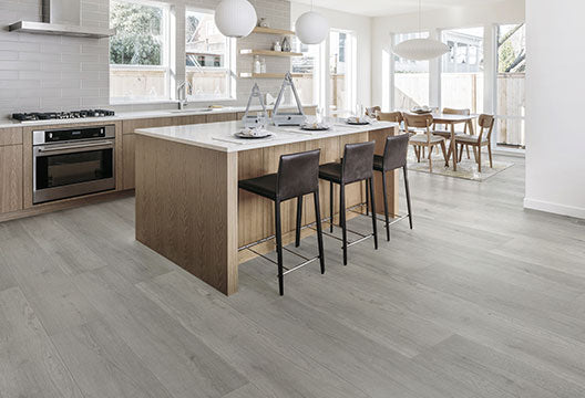 Modern open-plan kitchen and dining area featuring large-format grey timber-look floor tiles, timber cabinetry and white subway splashback tiles.