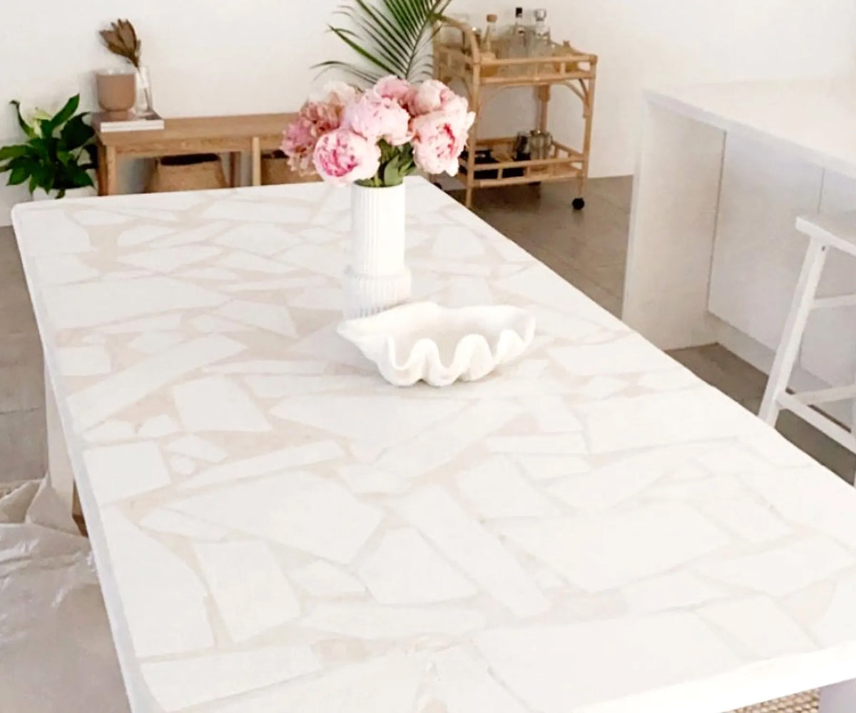 DIY tiled tabletop featuring a white terrazzo-style mosaic design, styled with a vase of pink flowers in a bright, modern dining space.