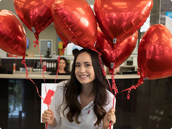 Beaumont Tiles team member celebrating in-store while holding red heart-shaped balloons, reflecting the company’s friendly culture and customer-focused approach.